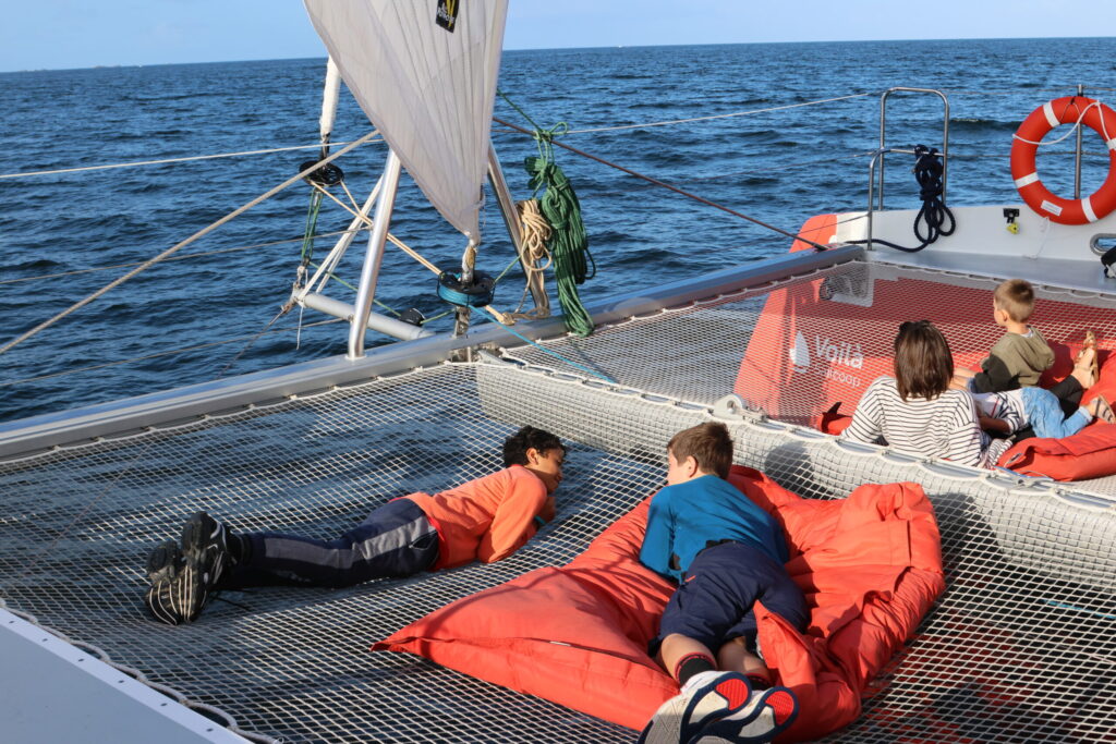 Enfants allongés sur le filet à l’avant du catamaran en route vers les Glénan, profitant de la traversée à la voile